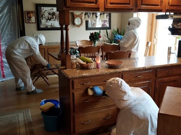 Technicians in protective suits cleaning a kitchen with containment sheeting up